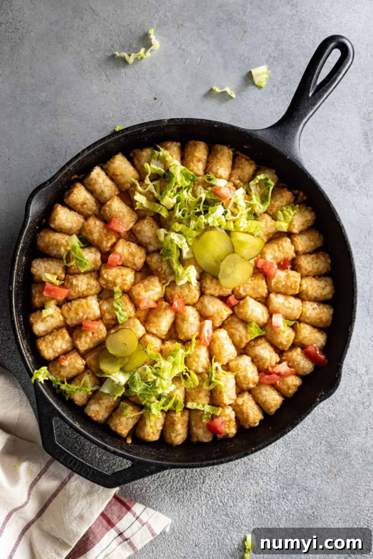 Overhead view of big mac casserole in a cast iron skillet garnished with pickles, tomatoes, and lettuce. 