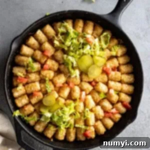 Overhead view of big mac casserole in a cast iron skillet garnished with pickles, tomatoes, and lettuce.