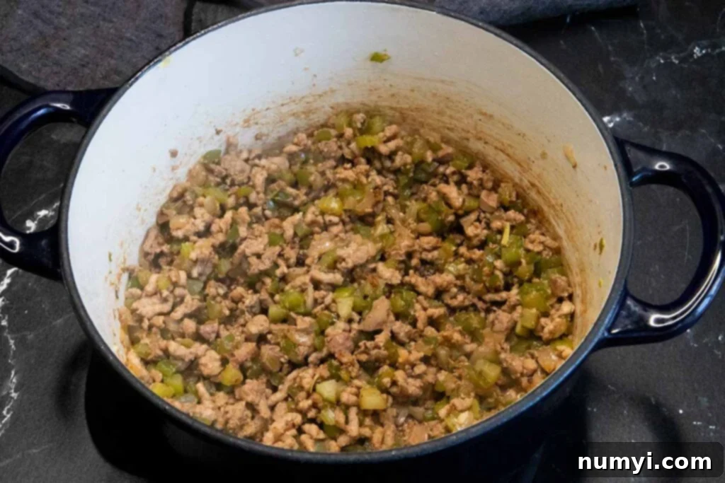 Close-up shot of the savory meat and vegetable mixture for Cajun dirty rice, cooked to perfection in a blue Dutch oven, showing the rich brown tones and aromatic steam.