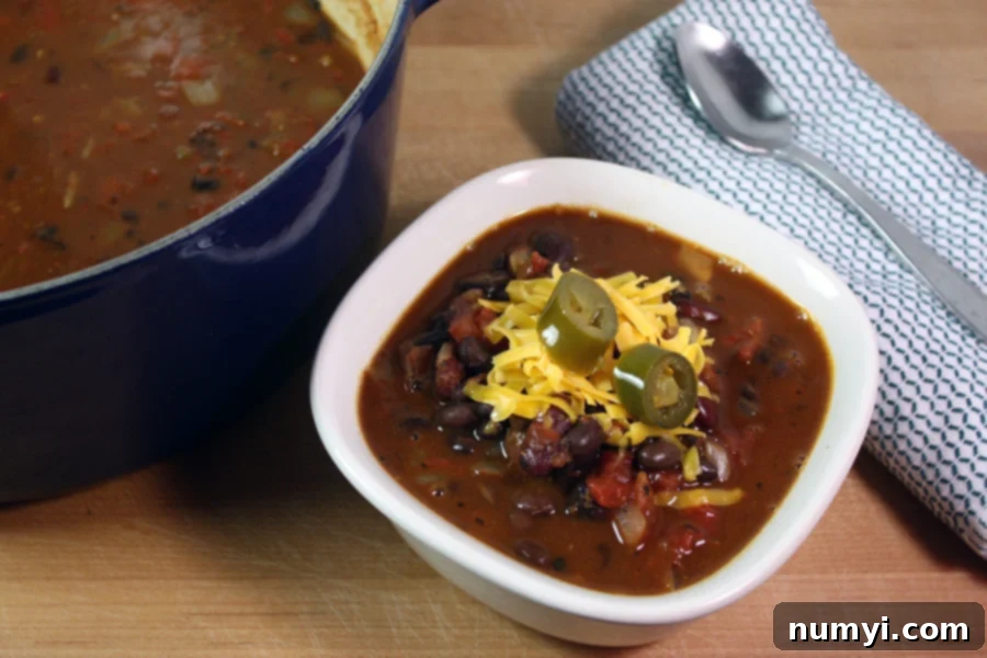 Vegetarian Chili in a white bowl garnished with shredded cheese and jalapeno slices.
