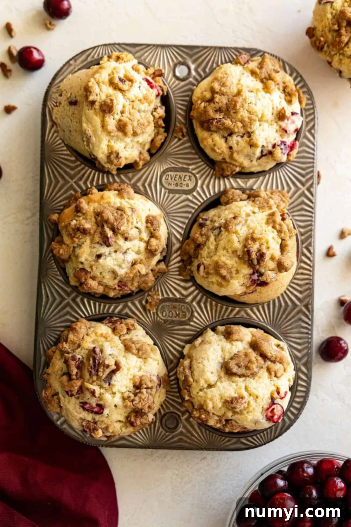 Overhead view of muffins in a muffin tin. Fresh cranberries scattered off to the sides and a red napkin in the corner. 