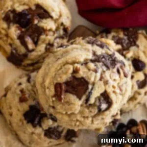 Close up of top of cookie. Dark red napkin in the corner. A small cup of dried cranberries and pecans in another corner.