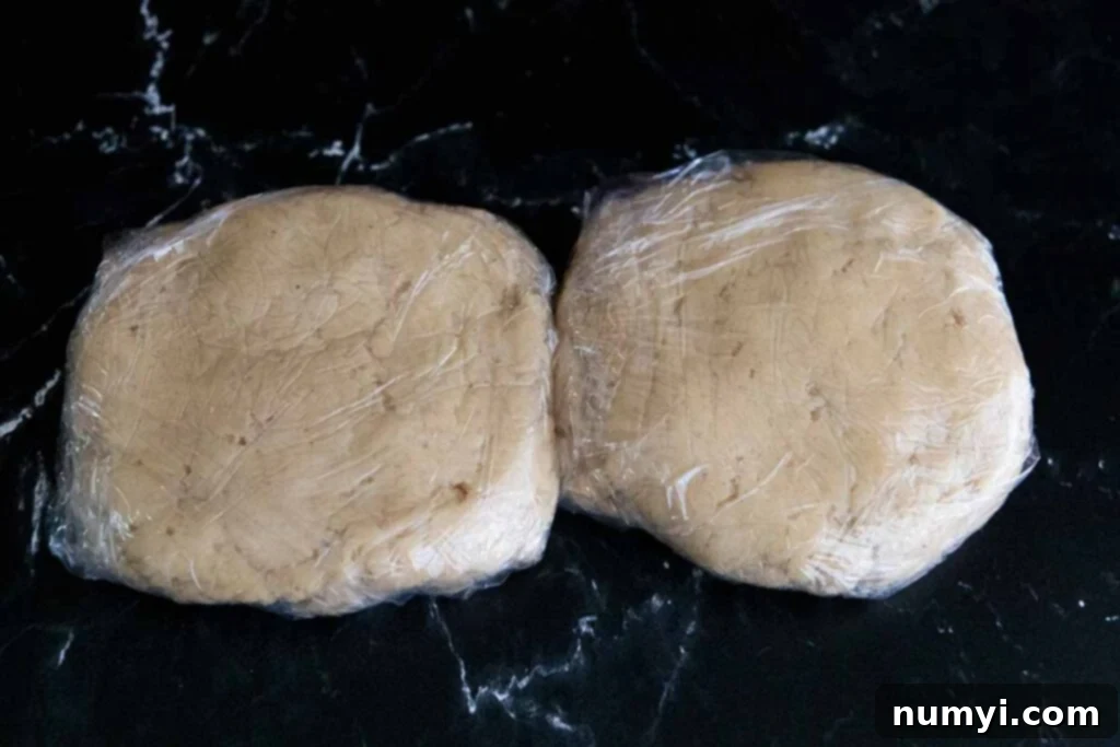 Two disks of eggnog cookie dough wrapped in plastic wrap, perfectly chilled and ready for rolling.