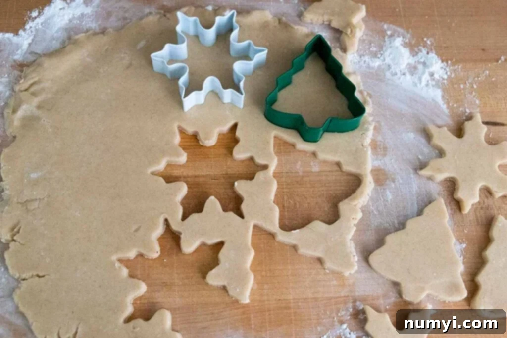 Various cookie cutters pressed into rolled-out eggnog cookie dough on a powdered sugar-dusted surface.