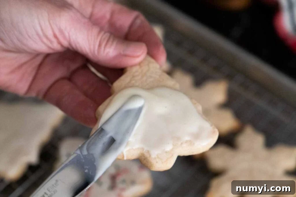 A baked eggnog cookie being delicately spread with sweet eggnog glaze using a butter knife.