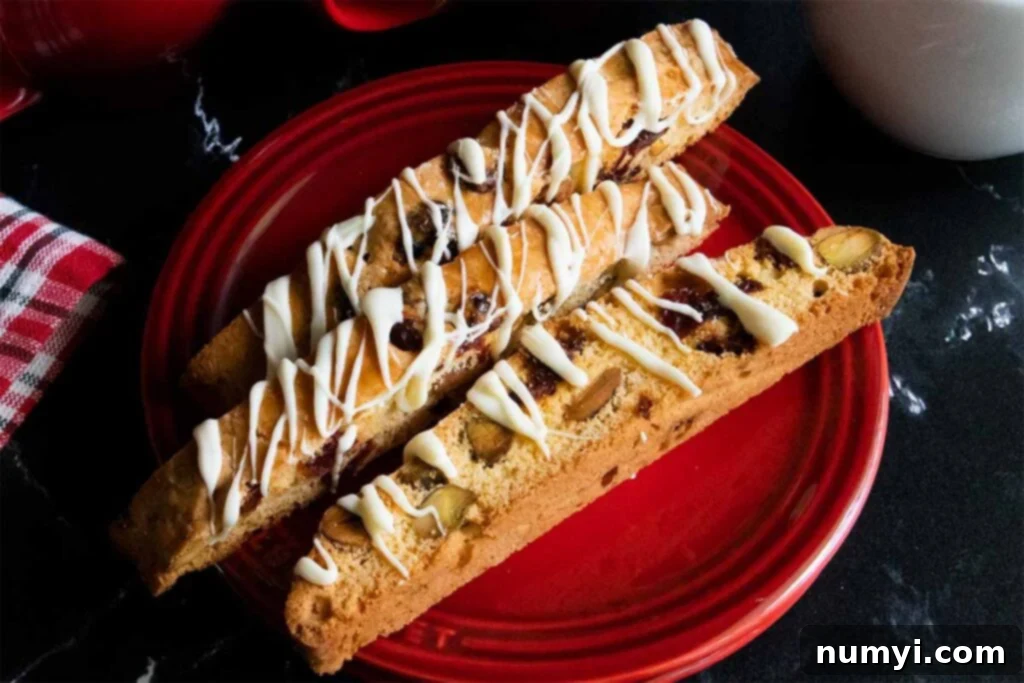 Exquisite White Chocolate Cranberry Pistachio Biscotti 2 Slices of white chocolate cranberry pistachio biscotti on a red plate.