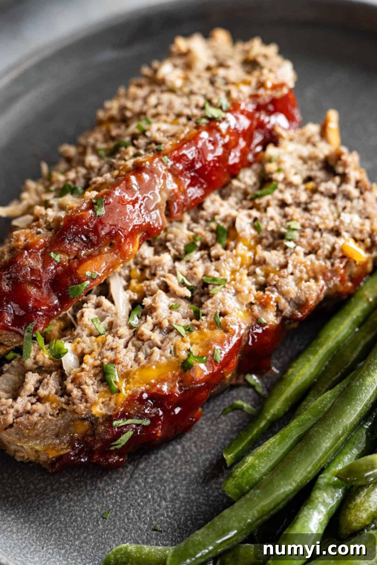 Close up shot of two slices of cheeseburger meatloaf with green beans on the side. 