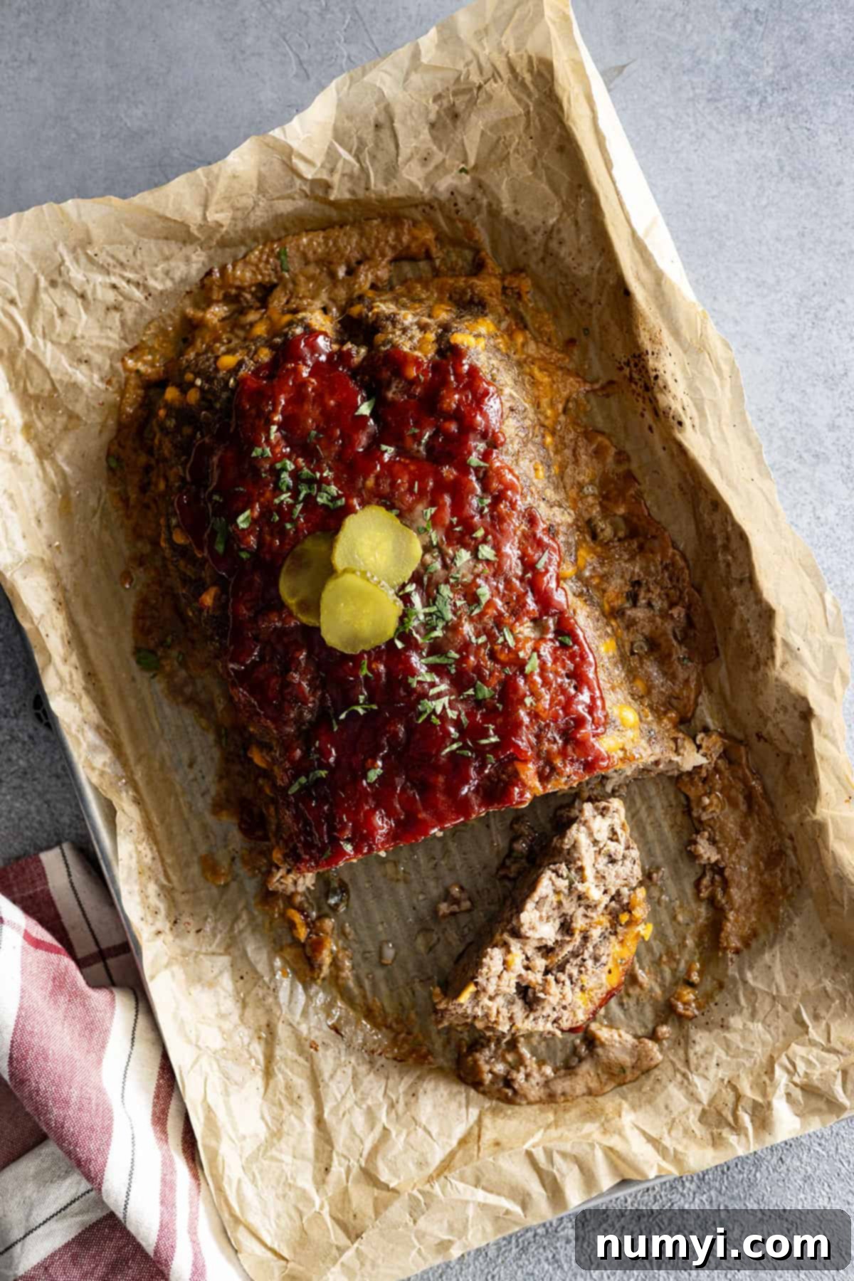 Overhead view of cheeseburger meatloaf from the oven. Garnished with pickle slices and minced parsley. 
