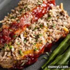 Close up shot of two slices of cheeseburger meatloaf with green beans on the side.