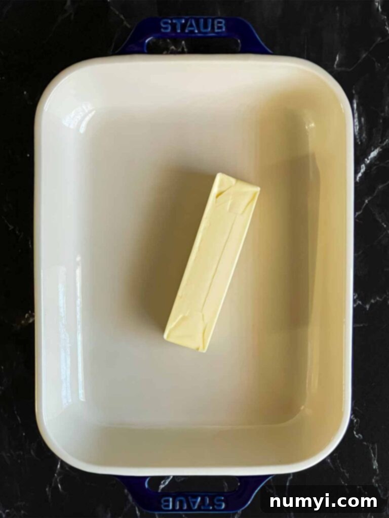 A full stick of butter melting in a glass casserole dish, warmed in a preheating oven, forming the rich base for the Basmati Rice Risotto.