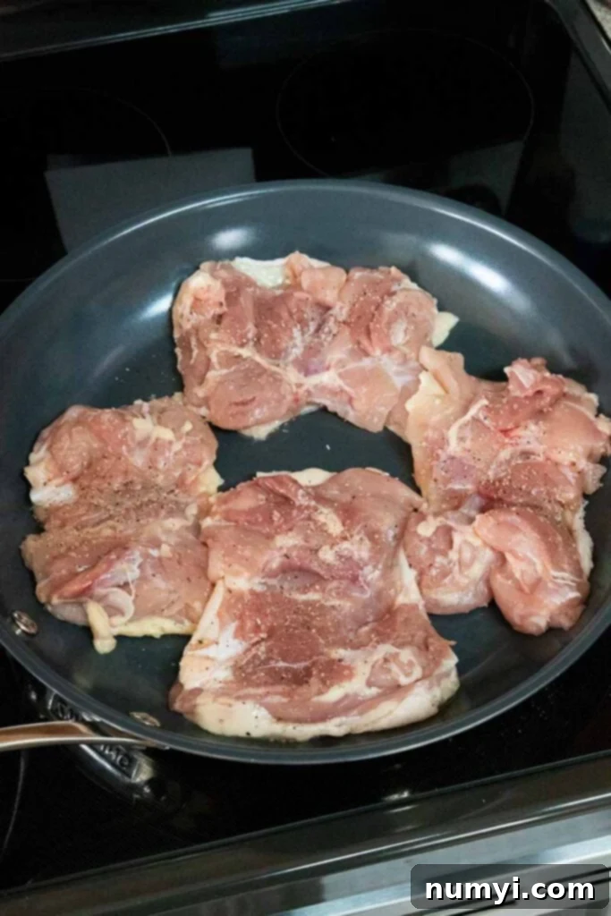 Raw chicken thighs seasoned with salt and pepper in a cold skillet, ready for cooking.