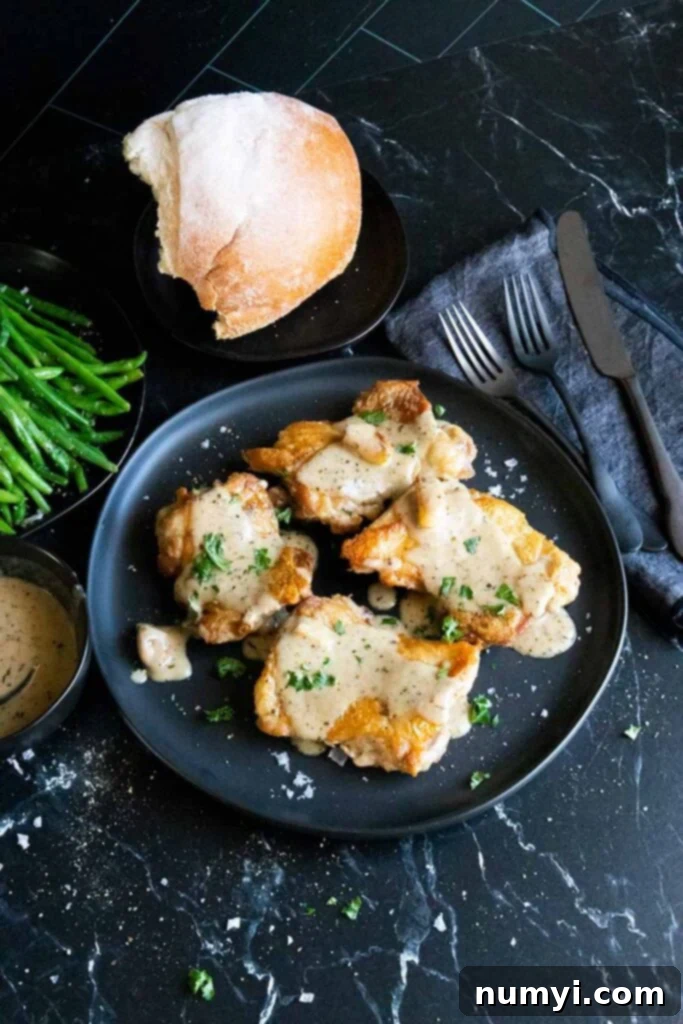 Crispy boneless chicken thighs drizzled with creamy garlic sauce, with bread and green beans in the background.