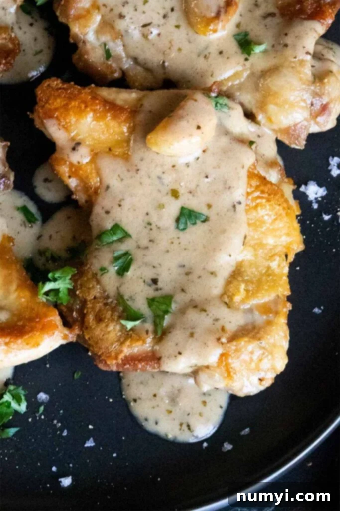 Close up of a crispy boneless chicken thigh with a creamy garlic sauce, highlighting the texture.