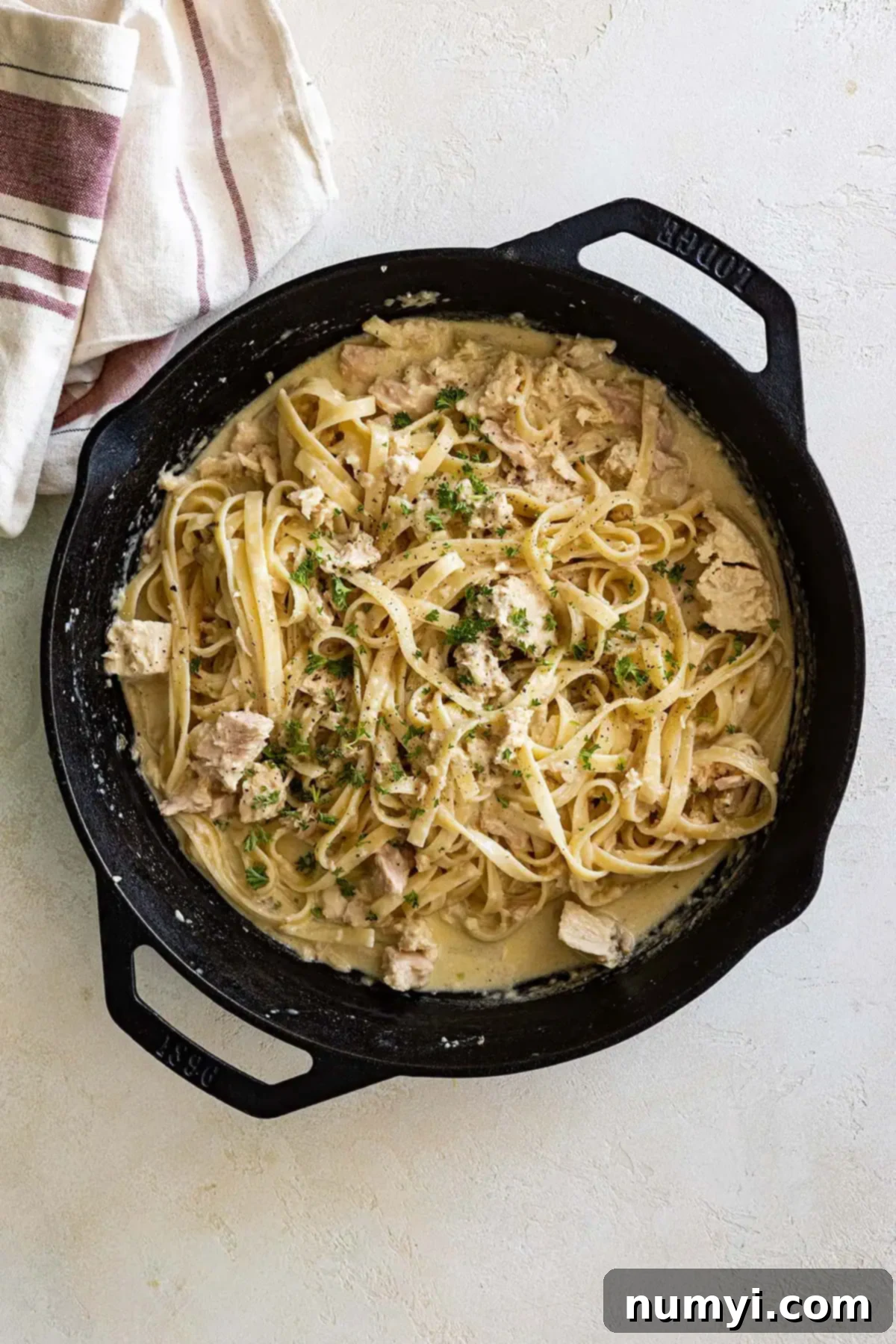 Overhead view of tuna alfredo in a large cast iron skillet garnished with fresh parsley. 