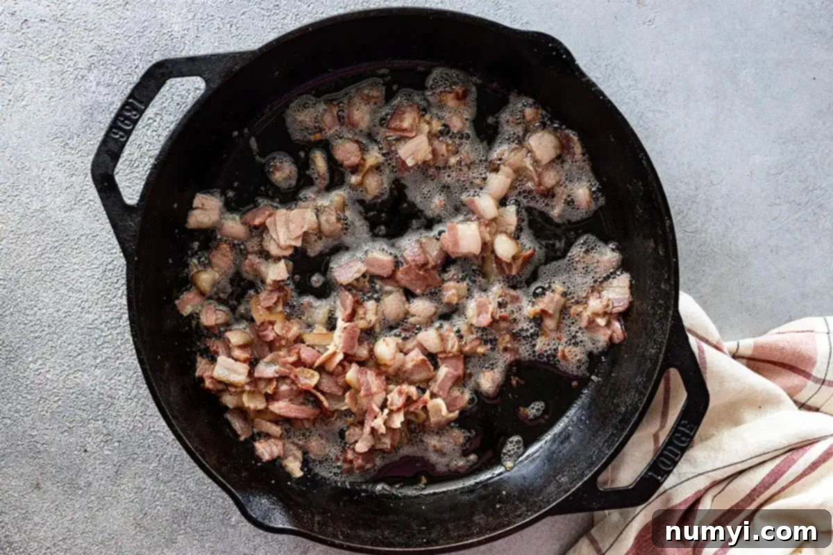 Overhead view of bacon frying in a large skillet. 