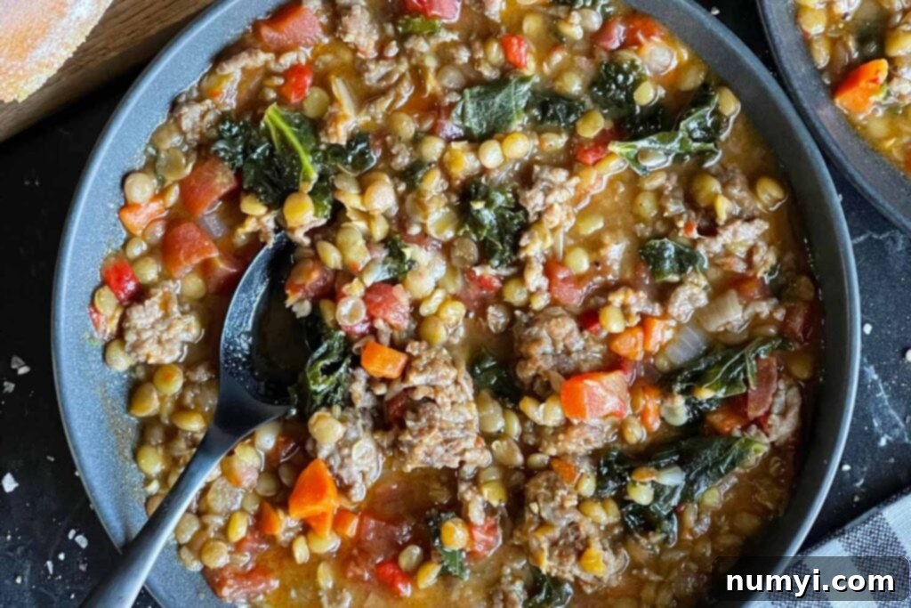Lentil soup with sausage and spinach in a dark bowl, ready to be enjoyed.