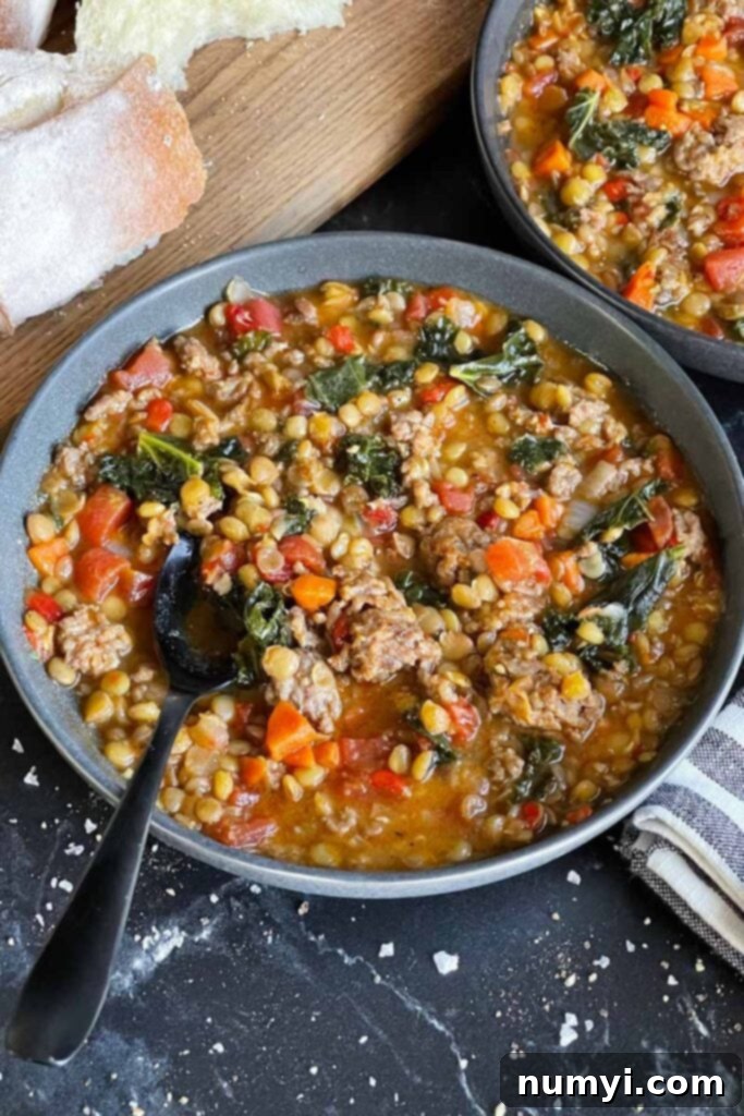 Two dark bowls of delicious Italian sausage and lentil soup, served with rustic bread on a wooden cutting board.