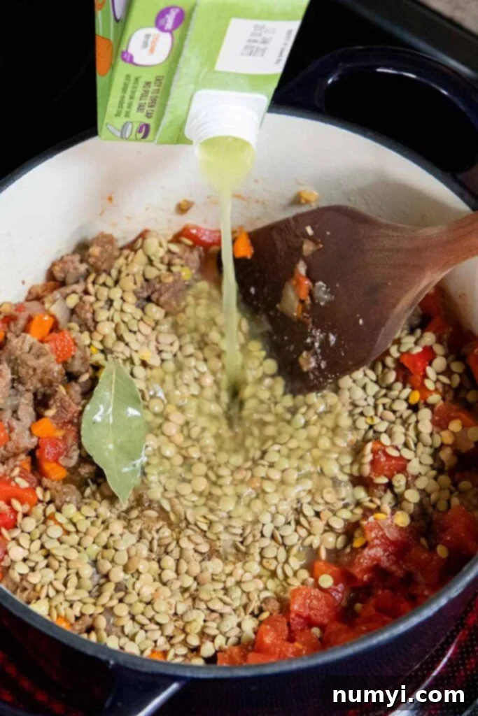 Soup ingredients in a dutch oven with chicken stock being poured in to create a rich broth for the lentil soup.