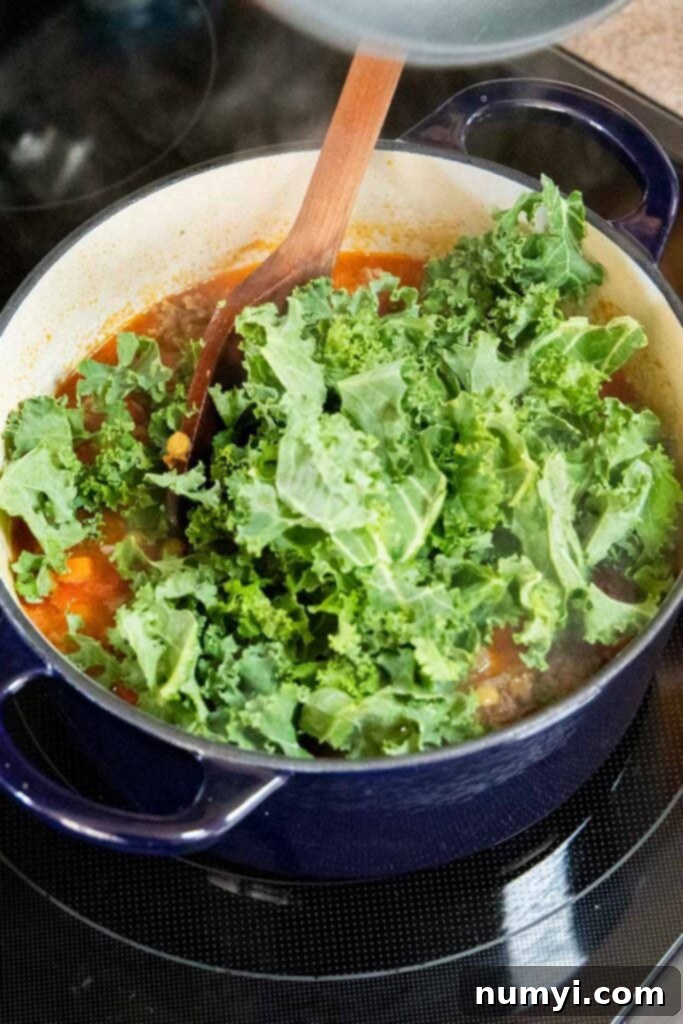 Fresh kale being added to a simmering pot of hearty lentil soup with Italian sausage.