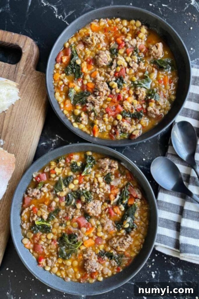 Two bowls of delicious and hearty lentil and sausage soup in dark bowls, with slices of rustic bread on a wooden board.