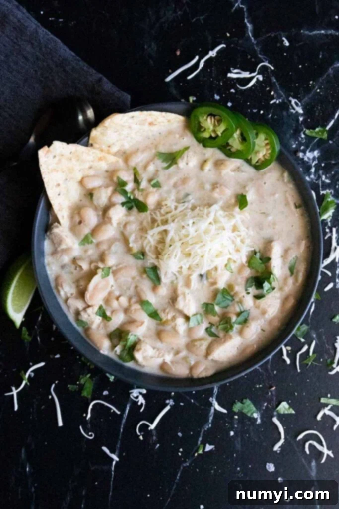 White chicken chili in a black bowl garnished with jalapenos, cilantro, tortilla chips and a lime wedge