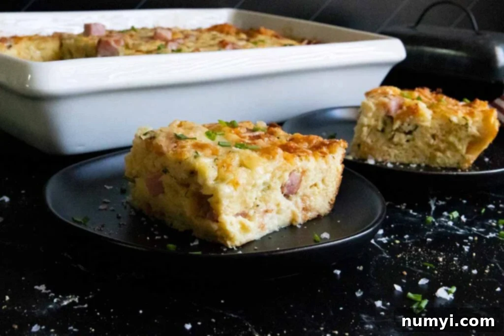 A perfectly baked slice of ham and cheese strata on a sleek black plate, showcasing its golden crust and delicious interior.