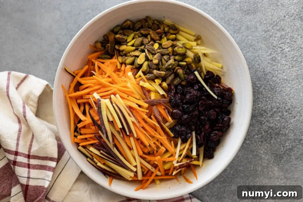 Sunshine Carrot Slaw 4 Overhead view of the carrot salad ingredients: julienned carrots, chopped pistachios, and dried cranberries, ready to be tossed with the creamy dressing in a large mixing bowl.