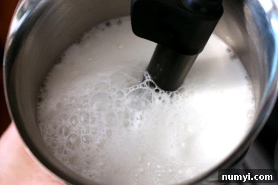 Craft Your Own Holiday Spice Flat White 8 Milk being skillfully steamed in a sleek metal frothing container, preparing for the flat white.