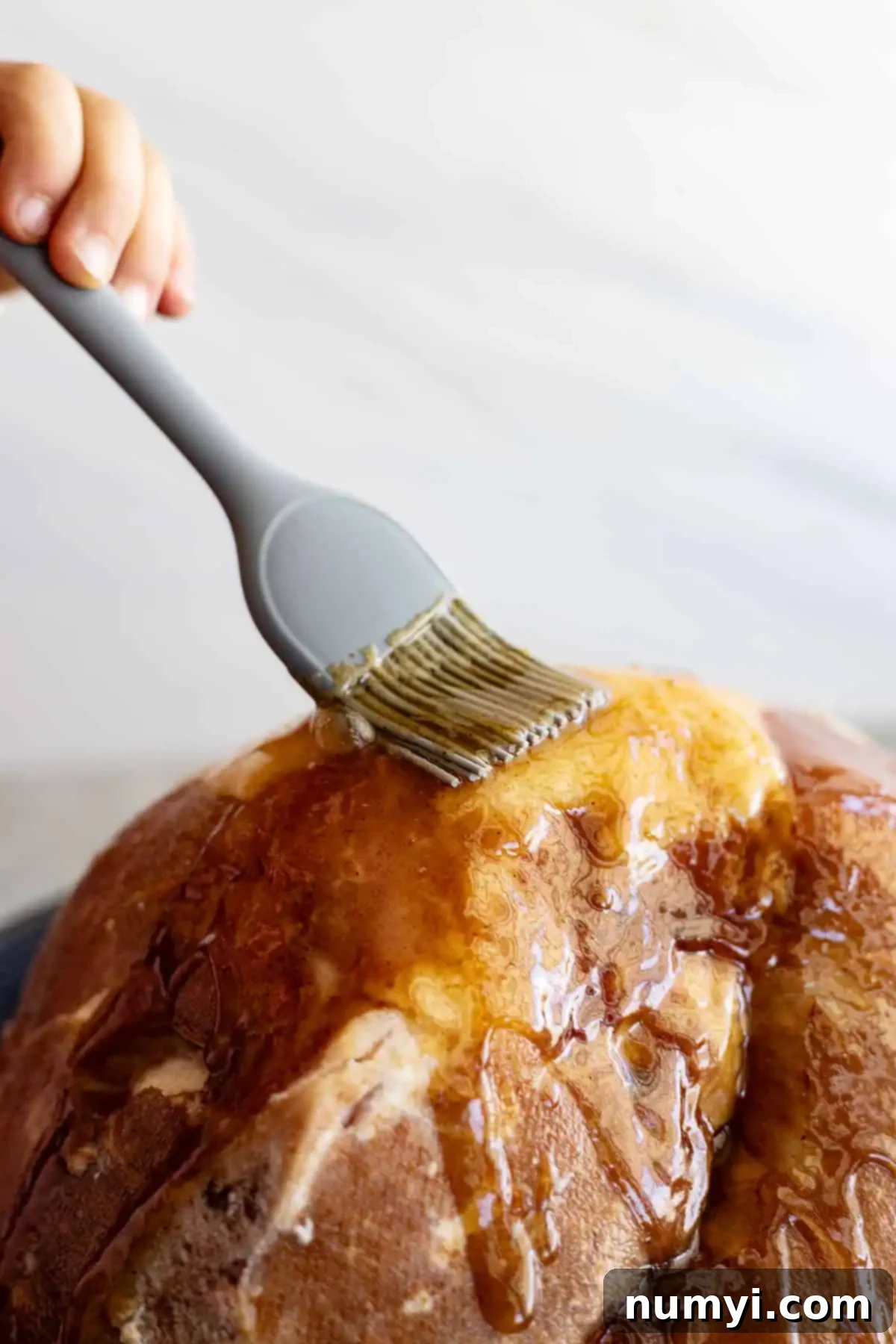 A brush adding glaze to a ham, creating a shiny, appetizing crust.