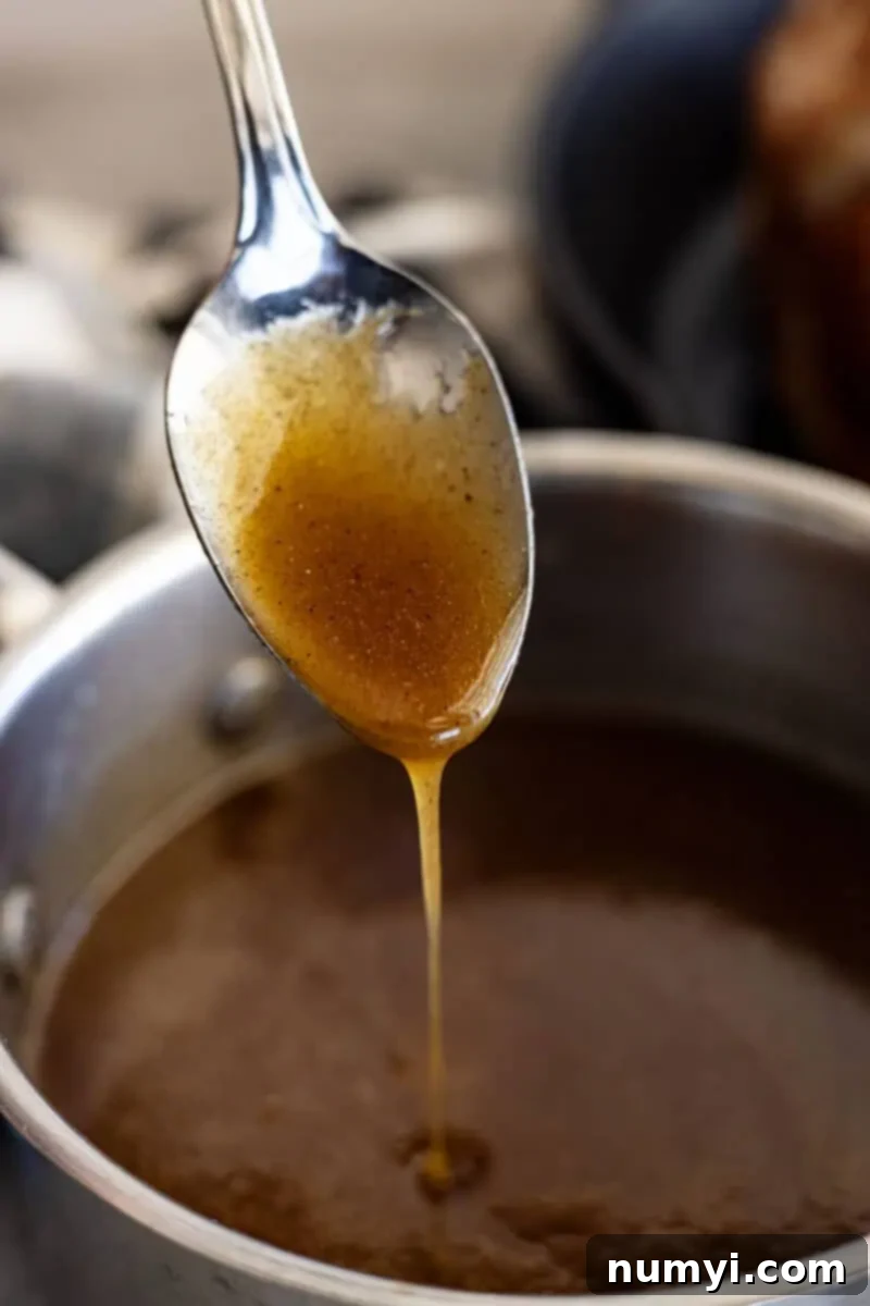 A spoon with honey ham glaze drizzling off into a pan, highlighting its rich, thick consistency.