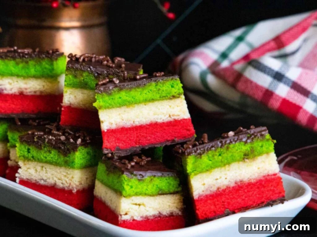 Vibrant Italian rainbow cookies neatly arranged on a white serving tray, showcasing their distinct red, white, and green layers with a glossy chocolate topping.