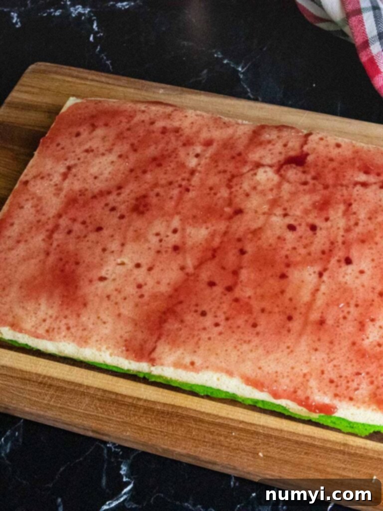 A thin, even layer of raspberry jam spread over the white (undyed) cookie layer, preparing for the final red cake layer to be placed on top.