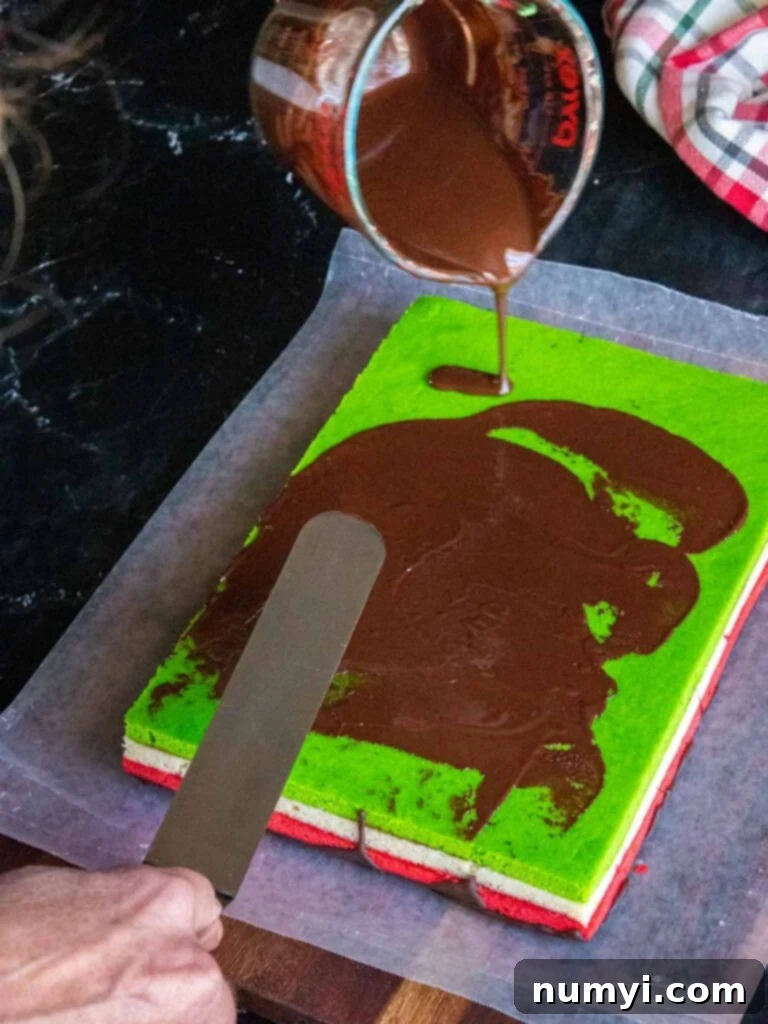 Melted chocolate being smoothly spread over the green bottom layer of the Italian rainbow cookie bar after flipping, ensuring even coverage.