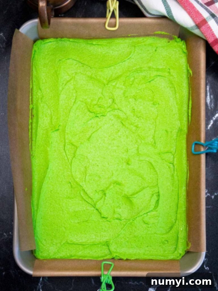 Vibrant green Italian rainbow cookie dough spread evenly in a parchment paper-lined baking pan, showcasing its rich color and readiness for baking.