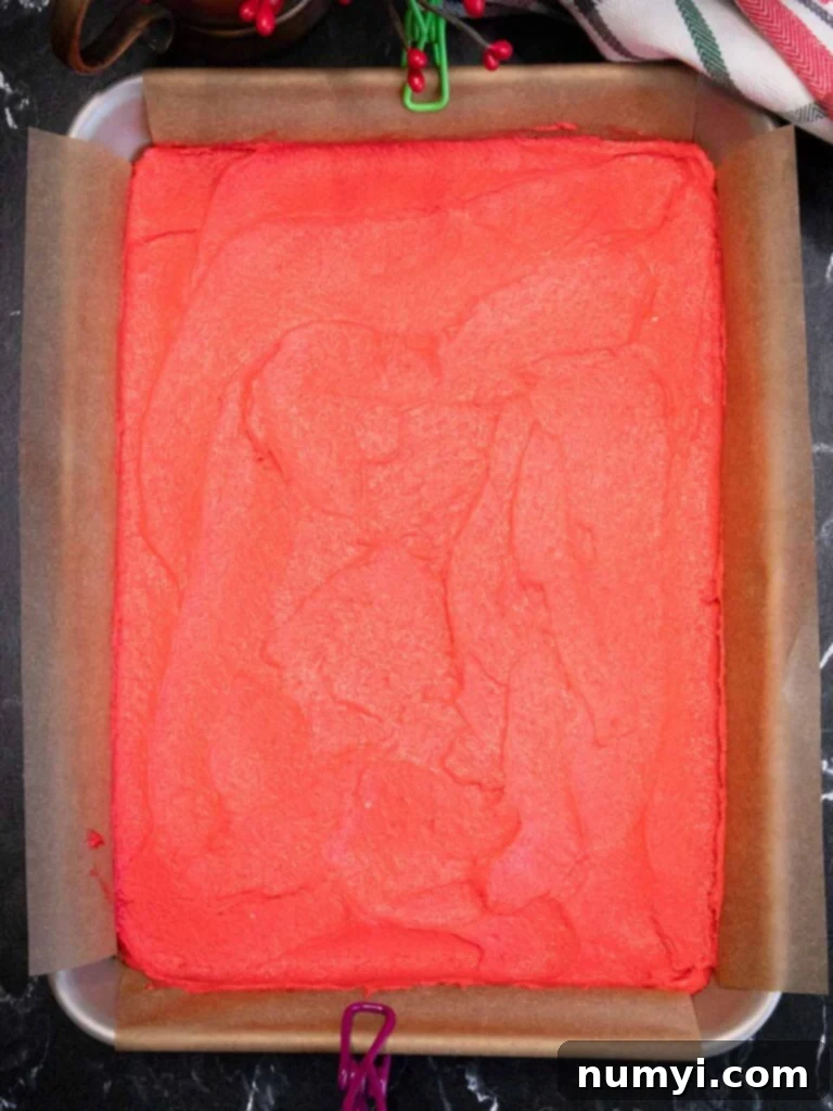 Bright red Italian rainbow cookie dough spread evenly in a parchment paper-lined baking pan, displaying its intense hue before baking.