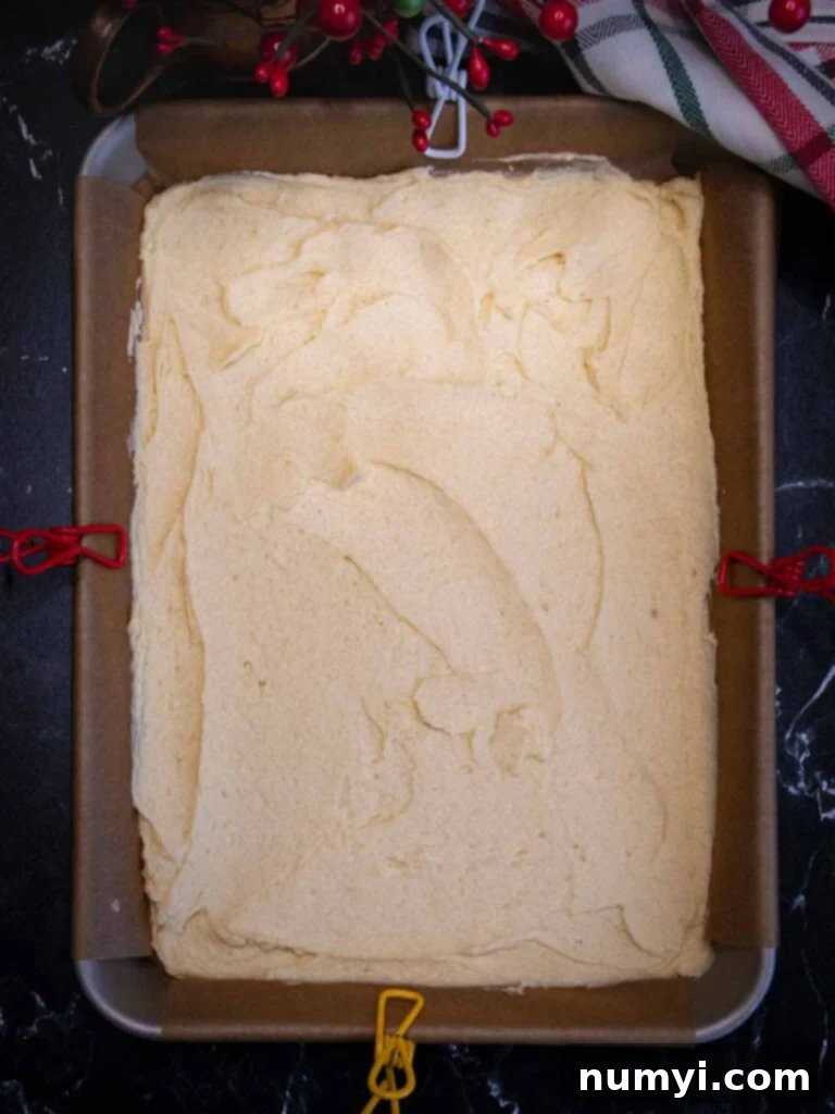 Uncolored (white) Italian rainbow cookie dough spread thinly and evenly in a parchment paper-lined baking pan, forming the crucial middle layer.