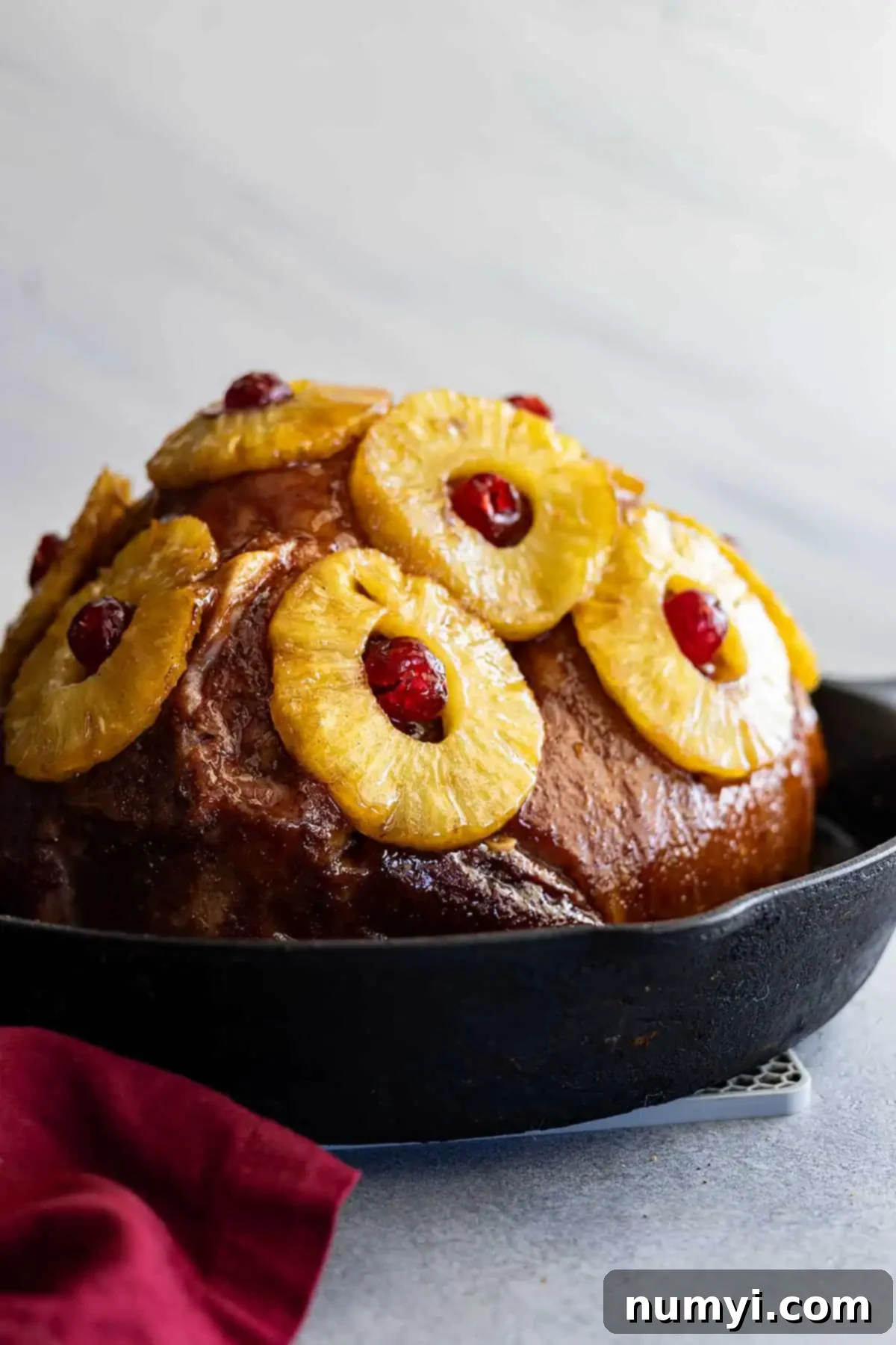 Pineapple ham in a cast iron skillet with red napkin off to the side. 