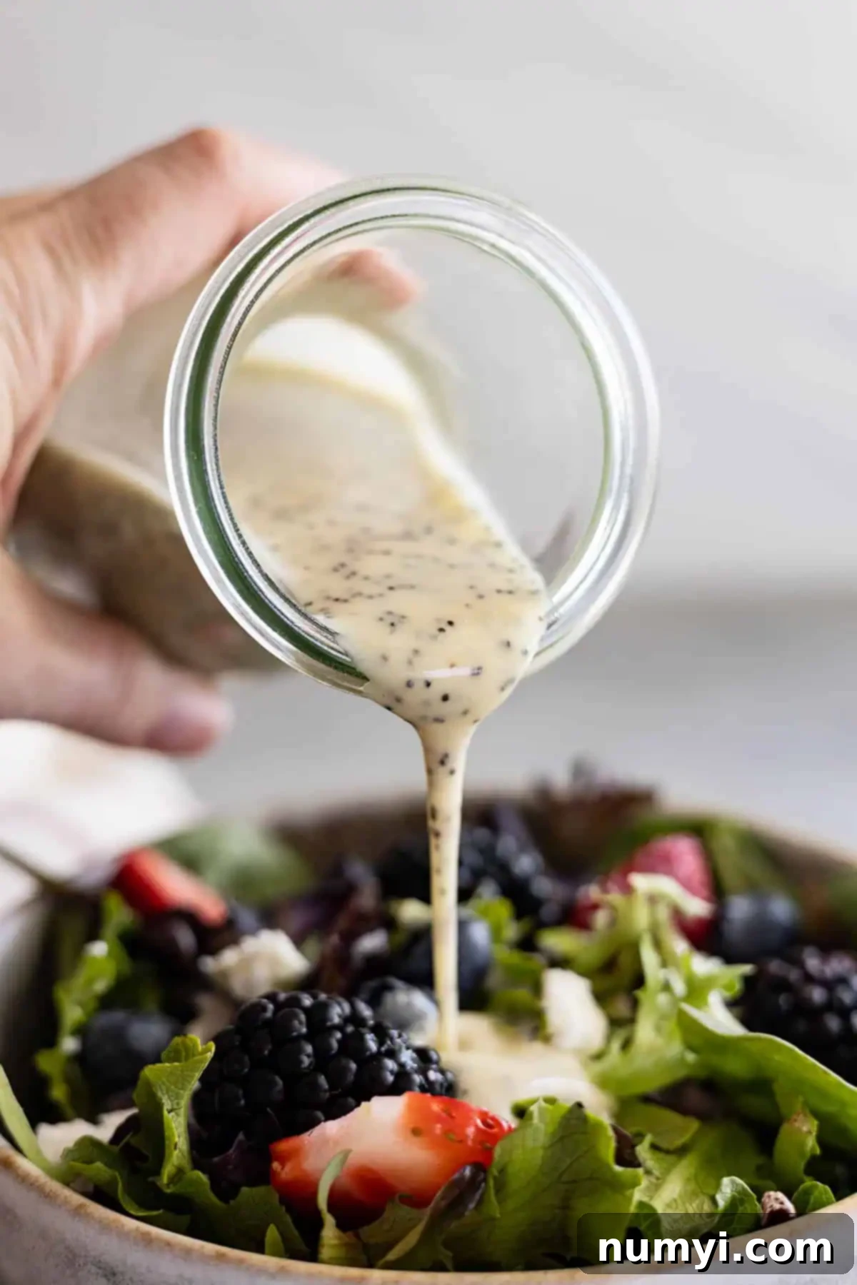 Bottle pouring dressing onto a berry salad.