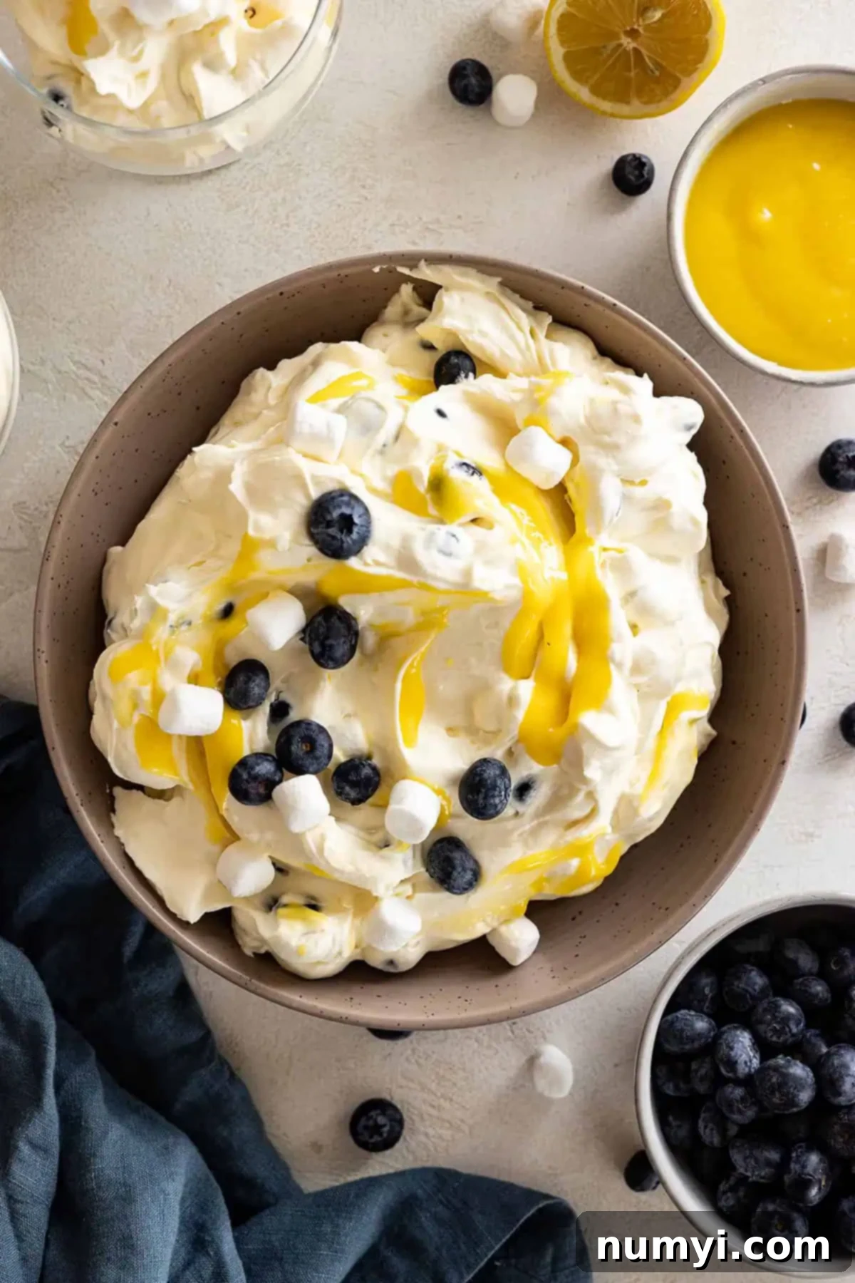 Overhead view of lemon blueberry fluff in a large bowl. Garnished with blueberries, marshmallows, and lemon curd. 