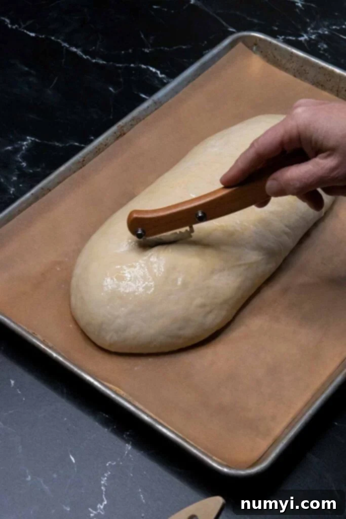 Making three diagonal cuts across the top of an unbaked Italian bread loaf with a sharp knife.