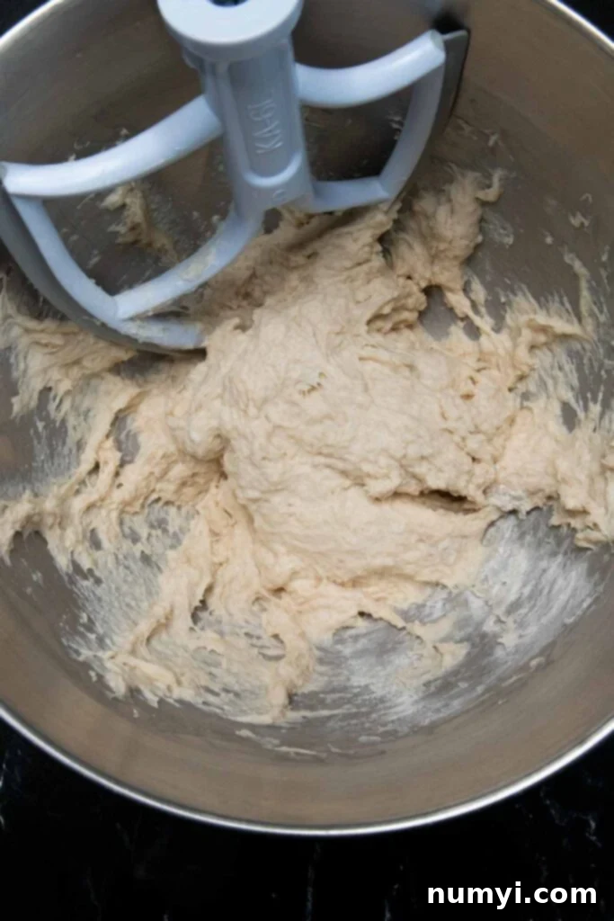 Initial dough ingredients mixing in a stand mixer bowl with the paddle attachment.