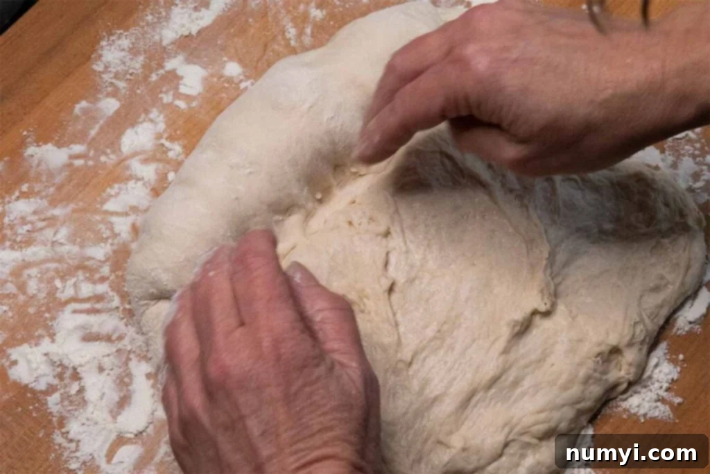 Rolling the flattened bread dough tightly into a compact, elongated loaf shape.