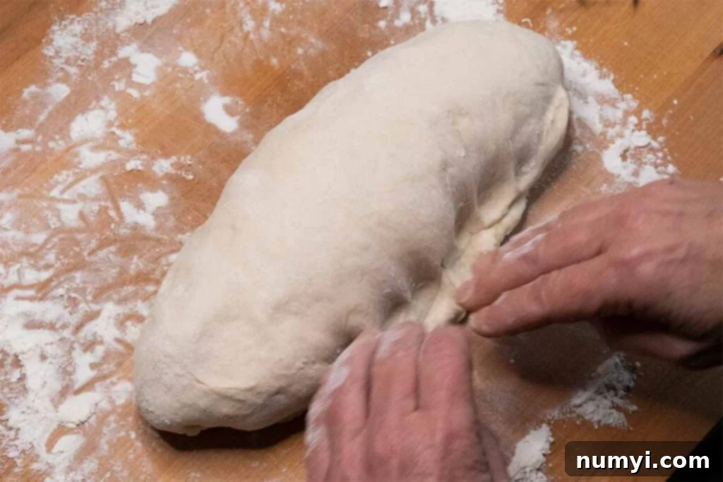 Pressing and sealing the seam along the bottom of the shaped bread dough to secure its form.