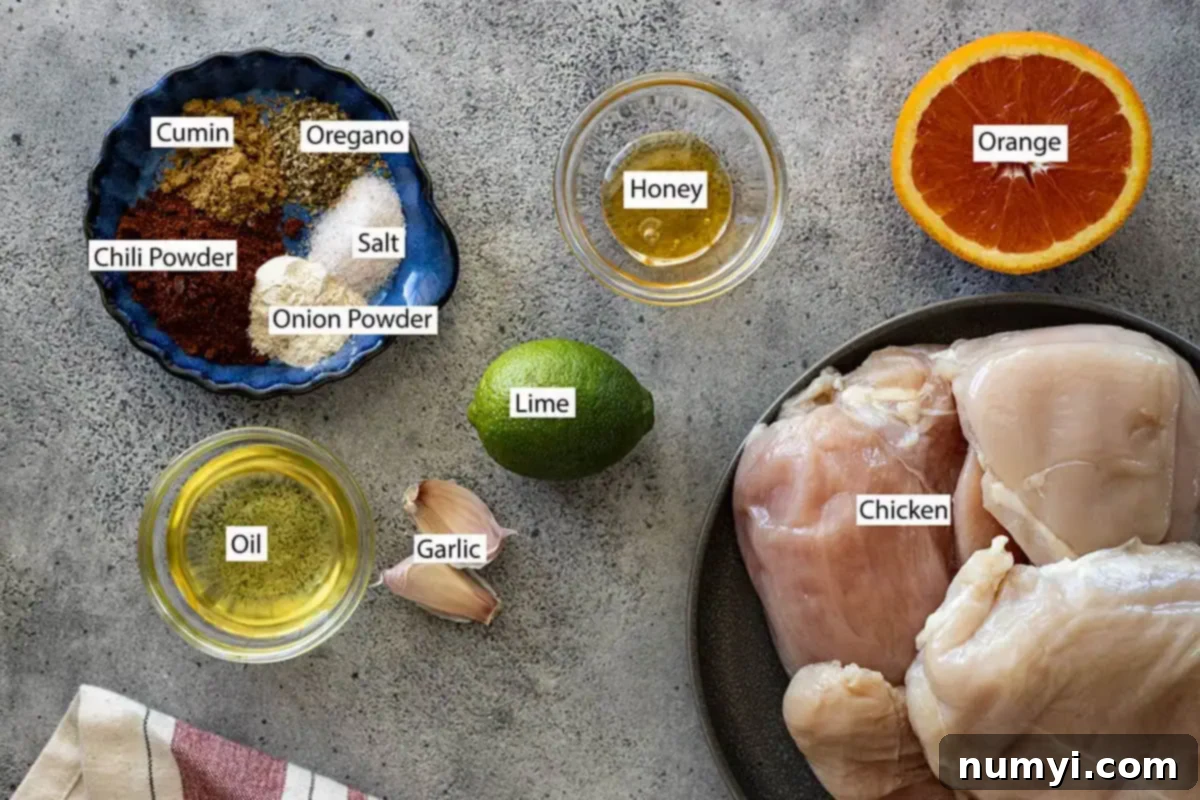 Ingredients for Mexican Chicken Marinade: fresh chicken, a vibrant array of spices including chili powder and cumin, fresh honey, bright lime and orange, pungent garlic, and a bottle of oil arranged on a rustic wooden surface.