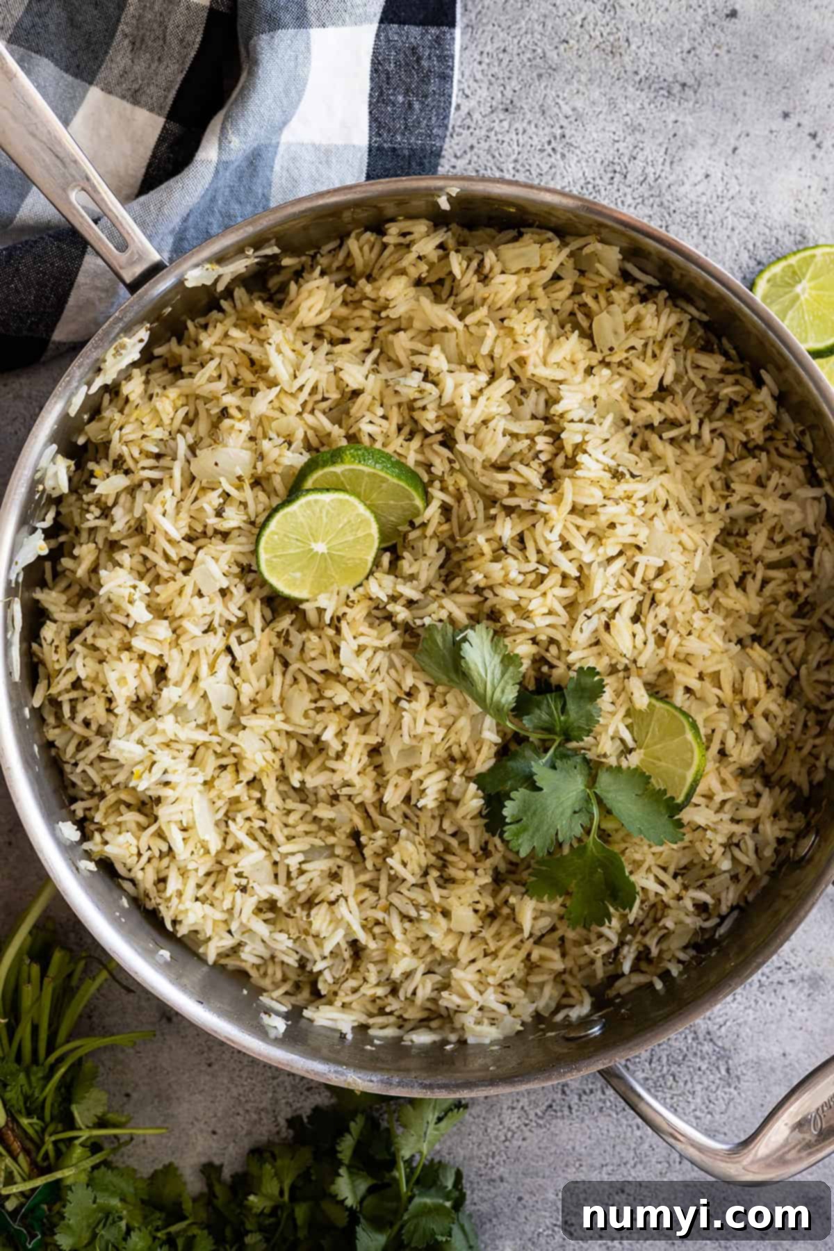 Overhead view of vibrant Mexican Green Rice in a skillet, beautifully garnished with fresh lime wedges and sprigs of cilantro, ready to be served.