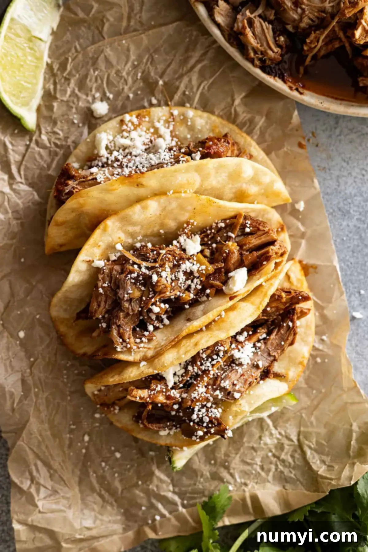 Overhead view of pork tacos on a piece of brown parchment sprinkled with cheese.