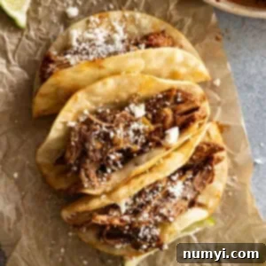 Overhead view of pork tacos on a piece of brown parchment sprinkled with cheese.