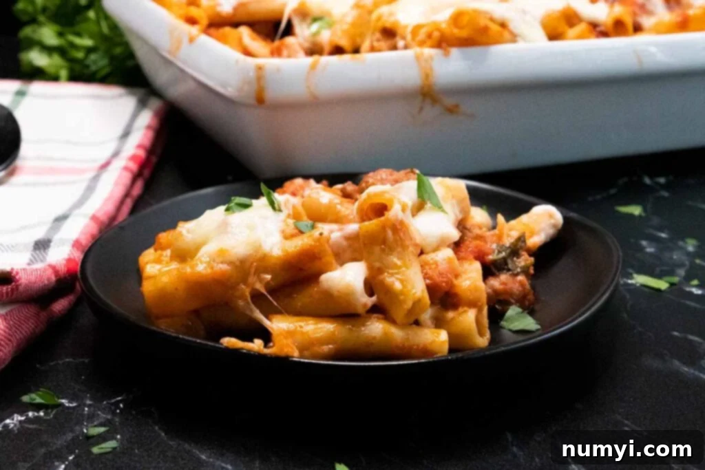 Baked ziti with a serving on a dark plate.