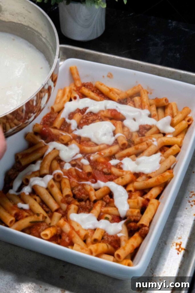 adding bechamel to the ziti casserole dish