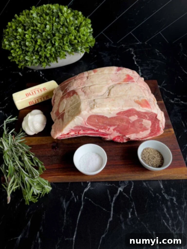 Closed Oven Prime Rib Roast 3 Ingredients for a herb butter prime rib rub, including butter, rosemary, garlic, salt, and pepper, arranged on a dark surface.